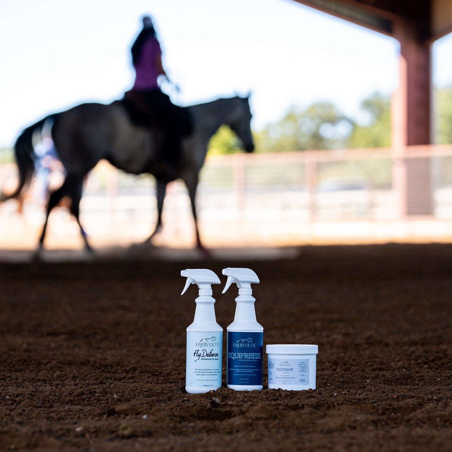 Three bottles of horse care products on a dirt ground with a horse in the background.